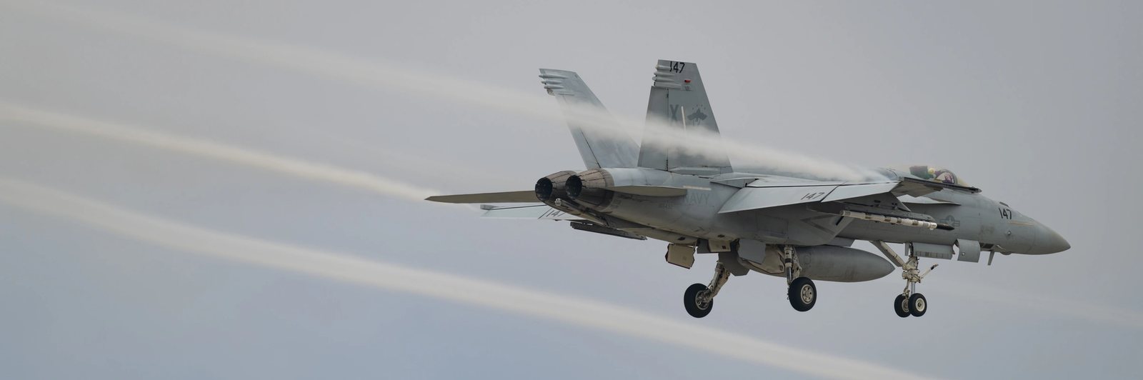 A fighter aircraft in flight, vapour streaming from its wing surfaces.